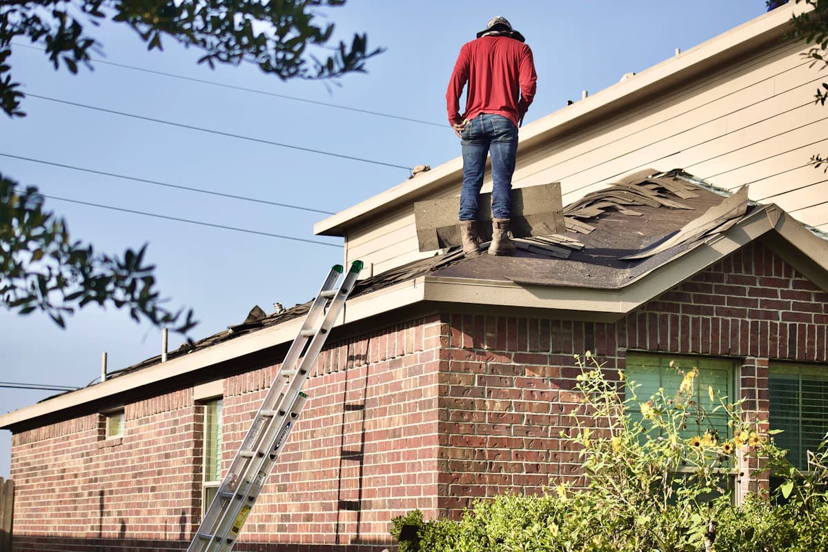 A roofer nailing down shingles on a residential roof under a clear sky